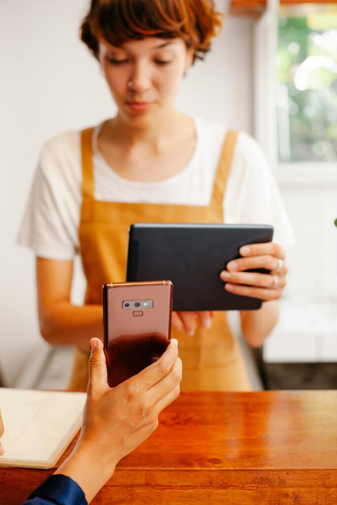 Two women using a smartphone and tablet in a bright indoor setting.